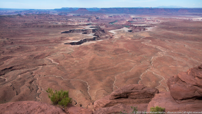 Pale drainage lines cross a red plateau toward distant mesas and ravines.