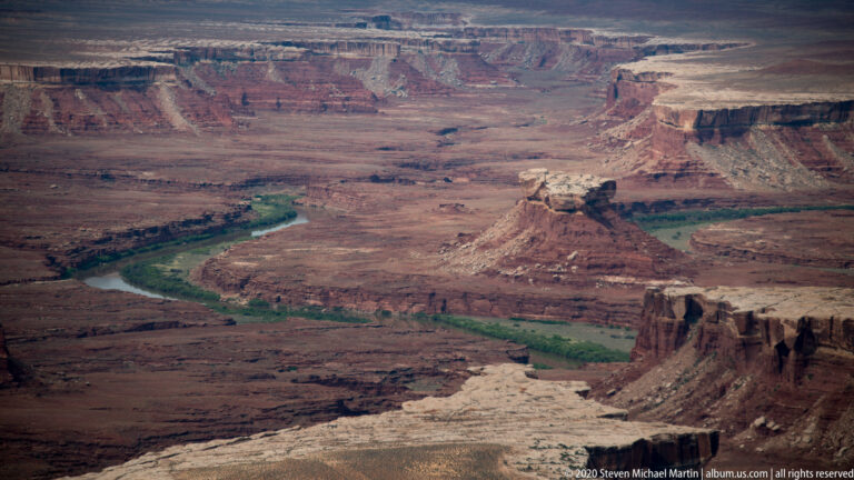 The Green River winds between high layered cliffs and a narrow green corridor.