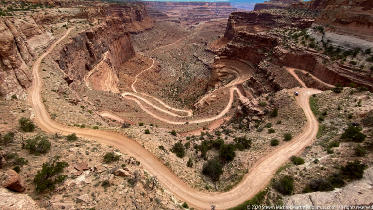 A winding dirt road crosses the canyon floor and climbs the opposite slope.