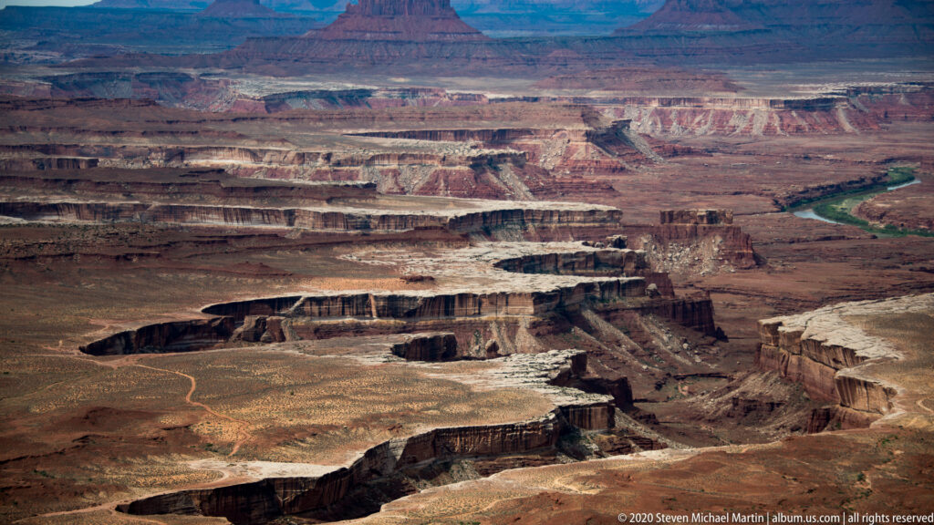 Tiered mesas and cliffs stretch toward a green river in the distance.