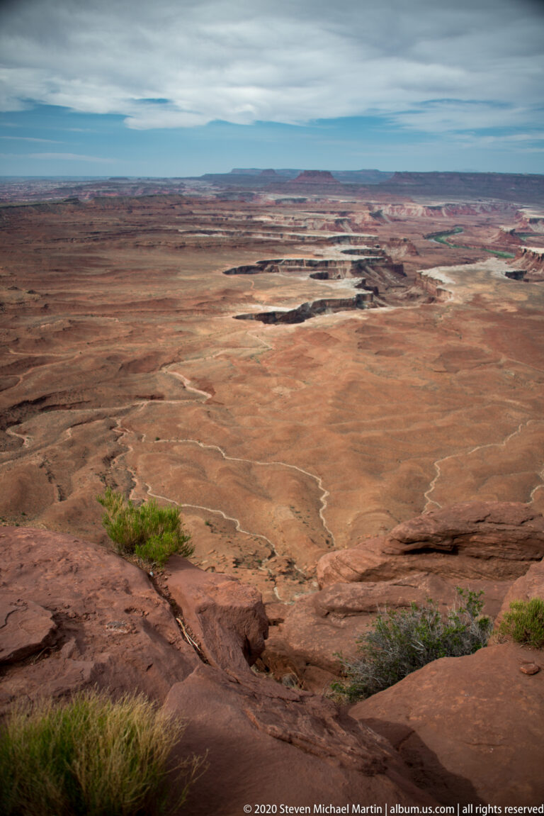 Pale winding drainages cross an open red plateau beneath distant mesas.