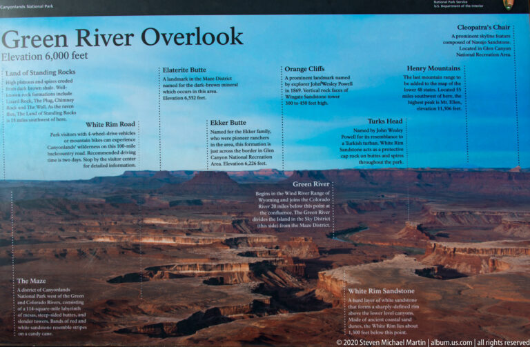 An overlook sign labels mesas and rivers across the canyon panorama.