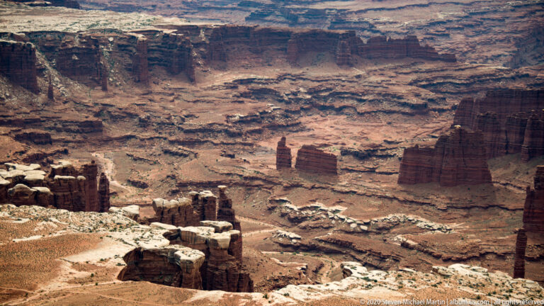Stepped mesas and red cliff bands rise above branching washes in a broad eroded basin.