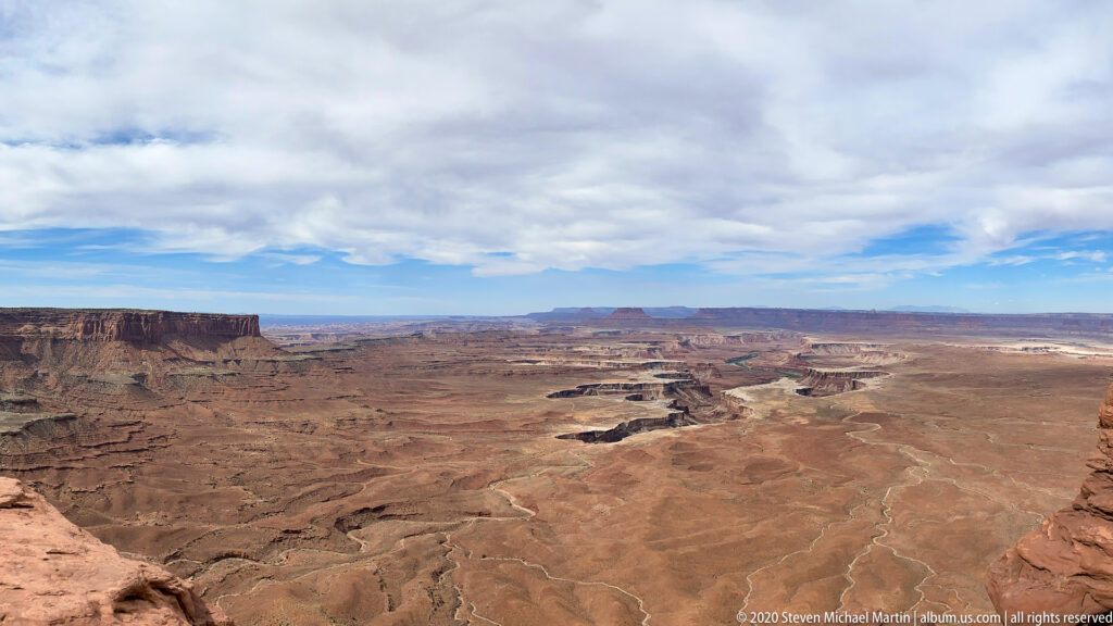 A cliff-edge view overlooks branching canyons and layered mesas beneath clouds.