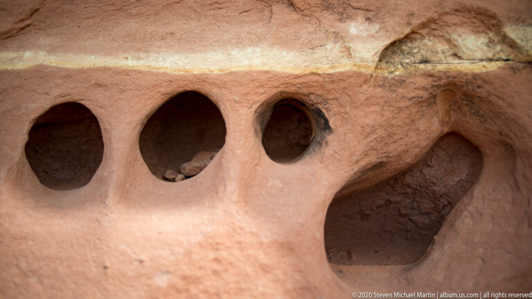 Three deep rounded cavities puncture a pale sandstone face, with smaller pits nearby.