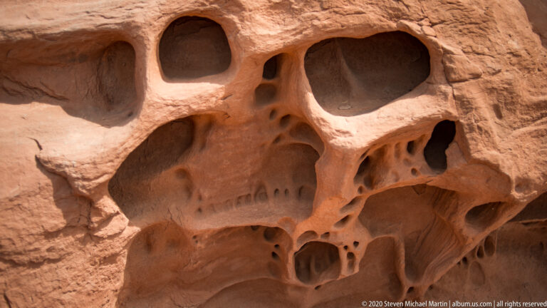 Large shadowed cavities and small pits create a deep relief in an orange sandstone surface.