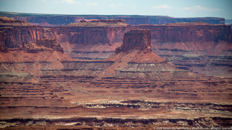 A steep-sided flat-topped butte rises from a broad basin of red and pale rock layers.
