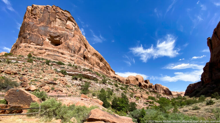 Steep sandstone walls enclose a narrow canyon passage, with a metal trail railing at lower left.