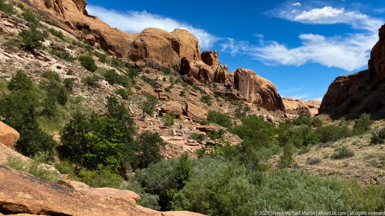 Pale sandstone cliffs form a narrow corridor with shrubs and broken rocks at their base.