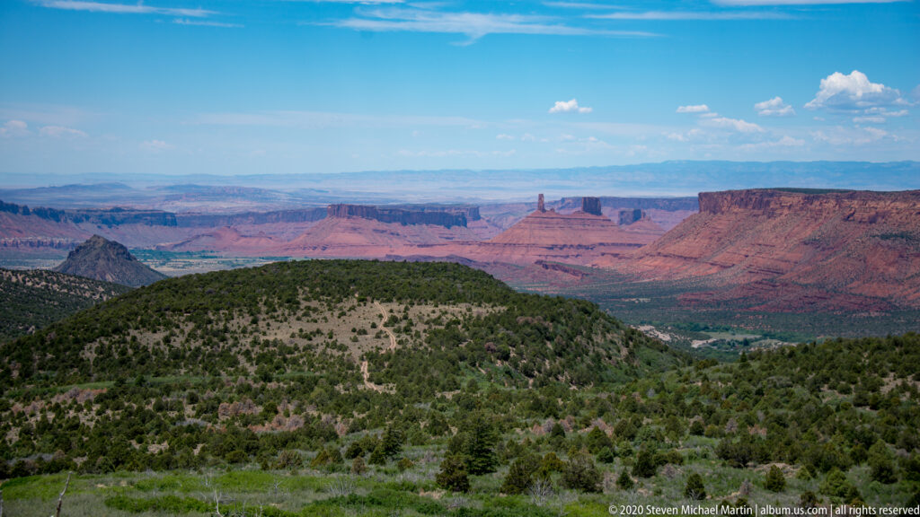 A sagebrush hillside leads toward distant red sandstone towers under an open sky.