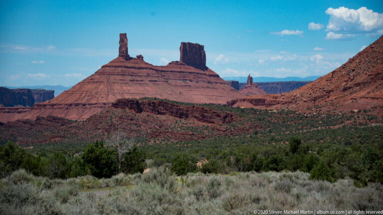 A narrow sandstone spire and a blockier tower stand side by side above a broad mesa.