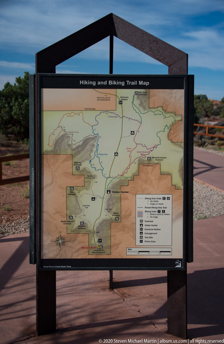 A trail map sign labeled “Hiking and Biking Trail Map” stands outdoors beside the surrounding landscape.