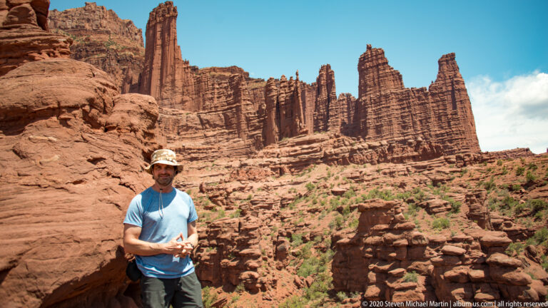 A visitor wearing a blue shirt and hat stands below the towering sandstone fins.