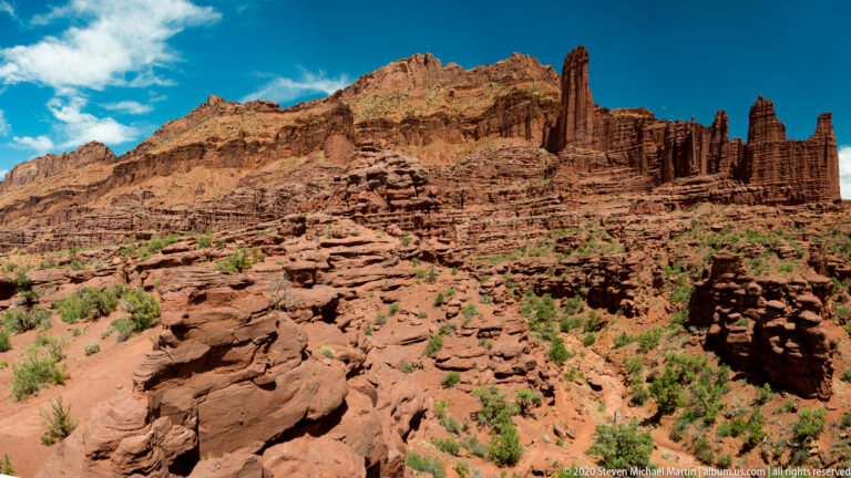 A wide sandstone ridge with spires rises above broken red rock and sparse vegetation.