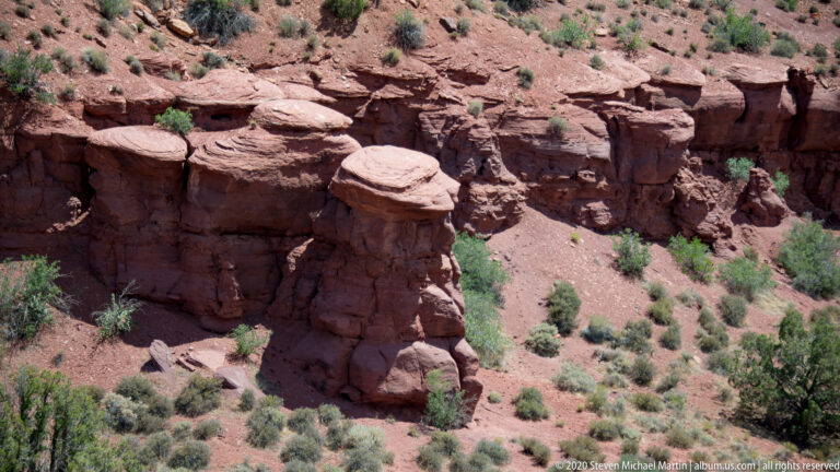 Blocky sandstone pillars and broken ledges cover a rocky slope dotted with shrubs.