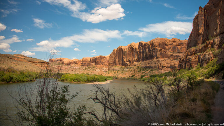 A river curves between dense green banks and sunlit red sandstone cliffs.