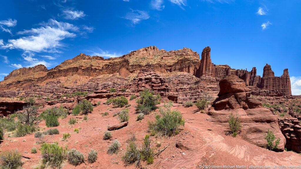 A red sandstone ridge with upright fins rises above low desert scrub and exposed earth.