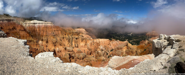 Orange and cream hoodoos descend into a broad amphitheater beneath a low bank of cloud.