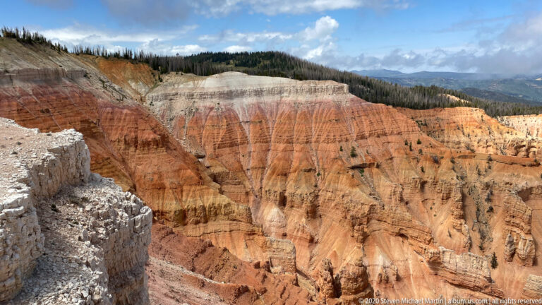 A banded pale-and-red cliff rises above orange pinnacles within the Cedar Breaks amphitheater.