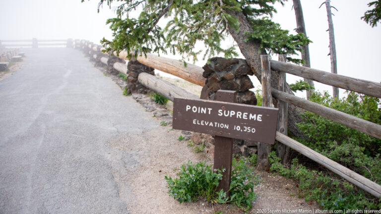 A Point Supreme sign gives an elevation of 10,350 feet beside a foggy road and timber guardrail.