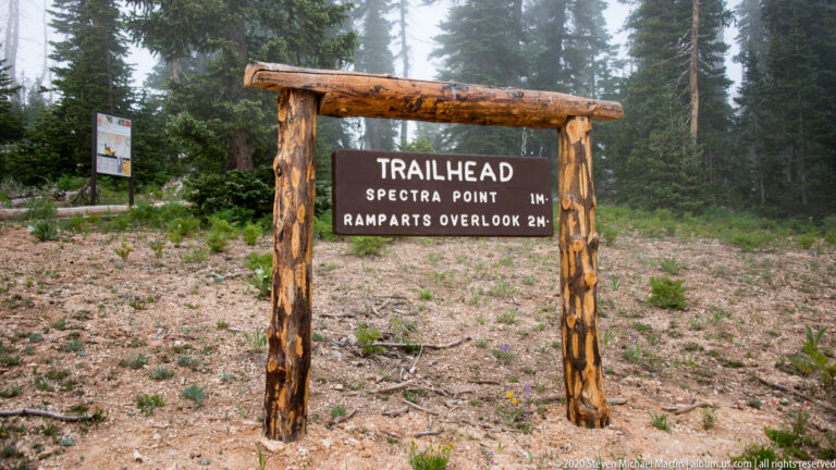 A timber trailhead gateway sign lists Spectra Point at one mile and Ramparts Overlook at two miles.