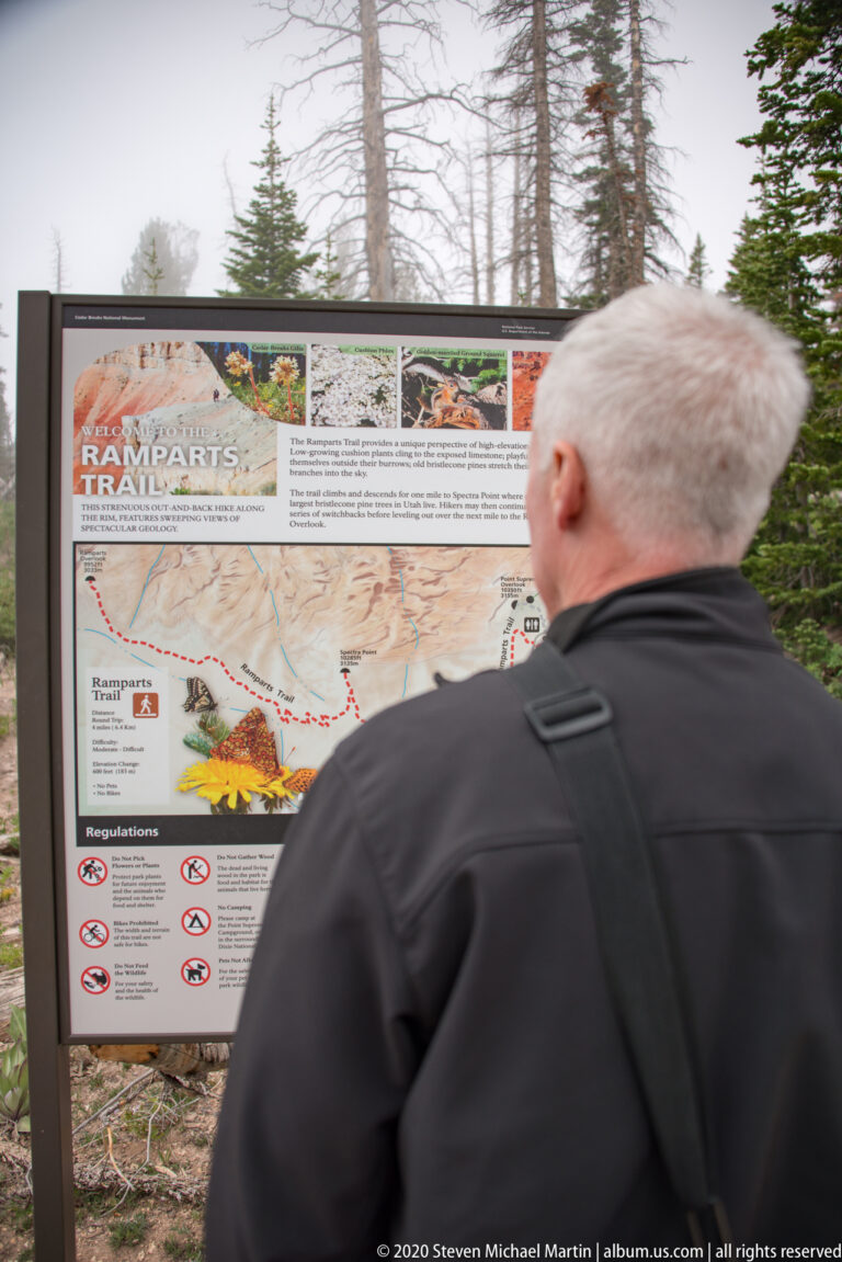 A visitor in a dark jacket reads a Ramparts Trail map and regulations panel.