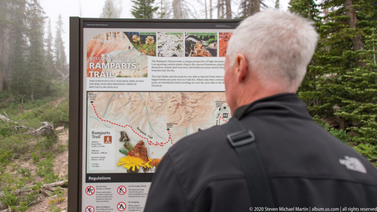 A visitor viewed from behind studies the Ramparts Trail map, partly obscuring its right side.