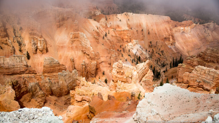 A closer view shows orange hoodoos and ridges beneath a fog-softened pale rim.