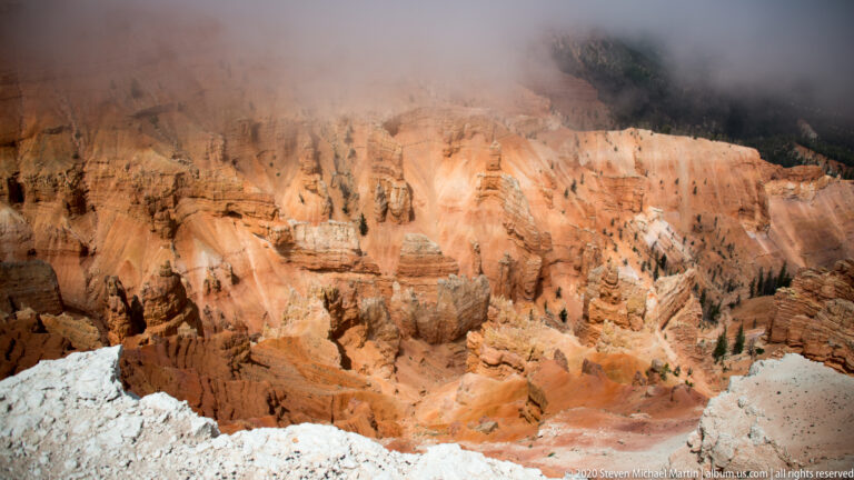A broad orange-and-cream hoodoo basin sits beneath low cloud, with a pale ledge in front.