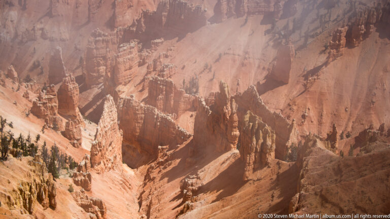 Narrow orange hoodoos stand above dark trees, fading into mist along the amphitheater rim.