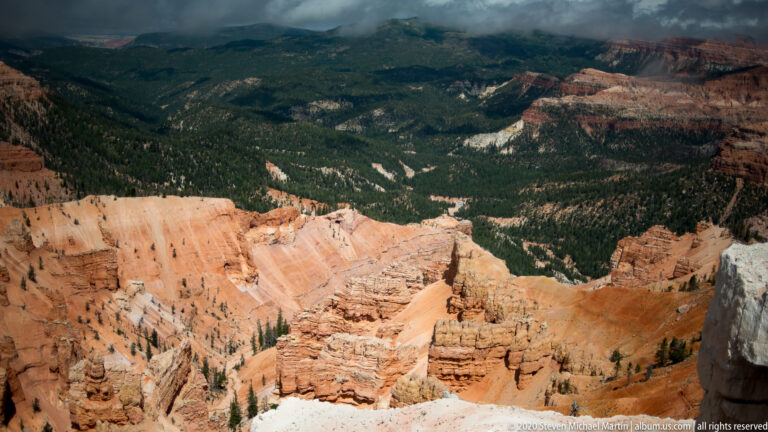Orange hoodoos and forested slopes spread beneath a high rim softened by cloud.