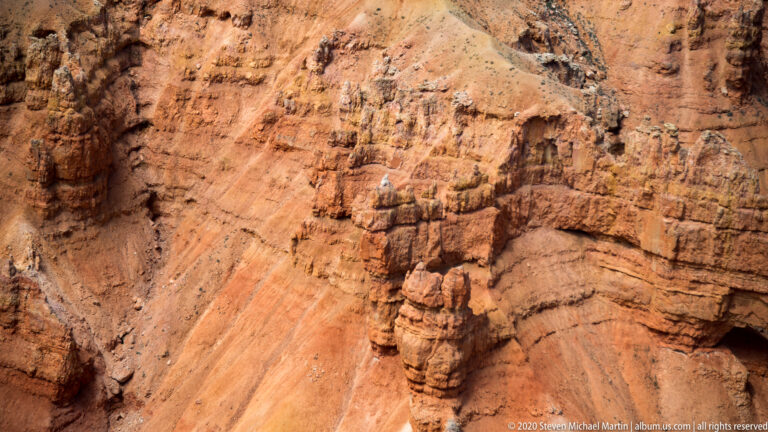 A banded rock pinnacle rises from a steep orange slope among neighboring formations.