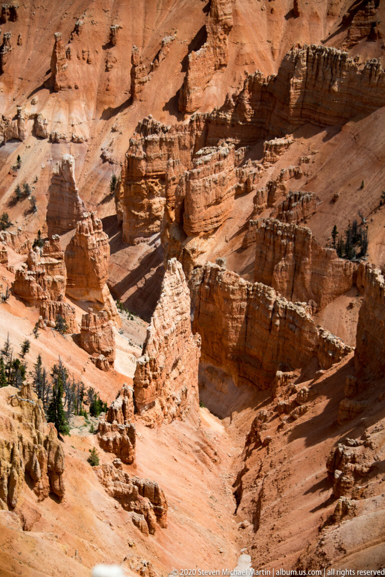 Narrow gullies divide an orange canyon slope into layered fins and hoodoo columns.