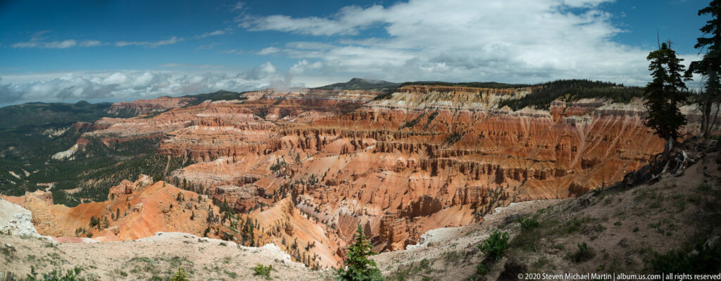 Clouds hang above orange hoodoos, pale slopes, and dark forested ridges across the amphitheater.