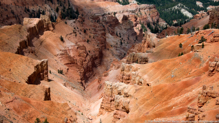 Orange gullies and pale channels descend between rock columns into a shadowed ravine.