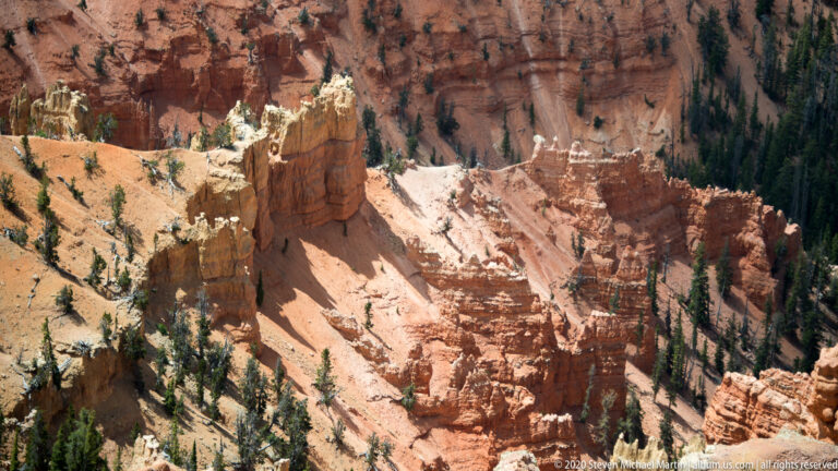 Layered columns rise above a pale slope beneath a dark forested rim.
