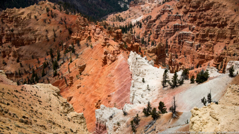 A pale slope with scattered conifers separates orange hoodoo ridges and dark canyon walls.