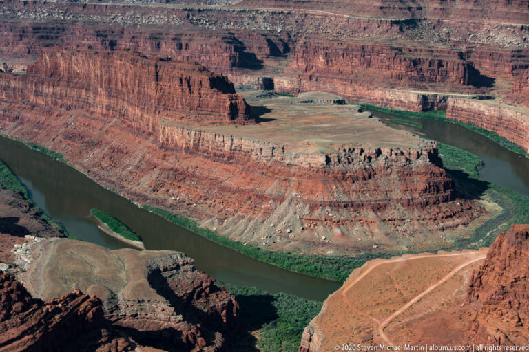 A green river loops around a red-rock peninsula between pale terraces and steep canyon walls.