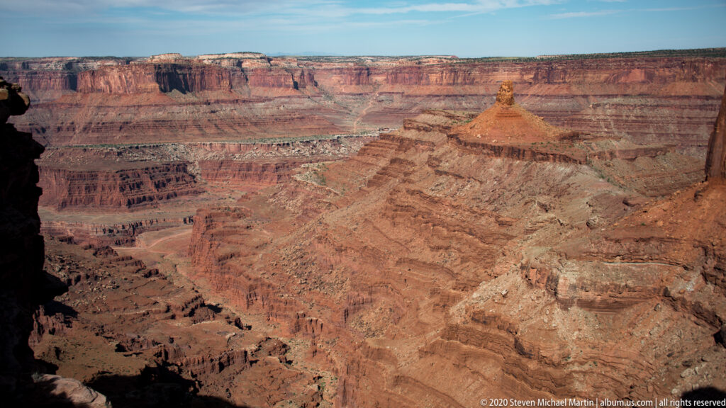 Layered red and pale canyon walls descend toward an isolated flat-topped butte.