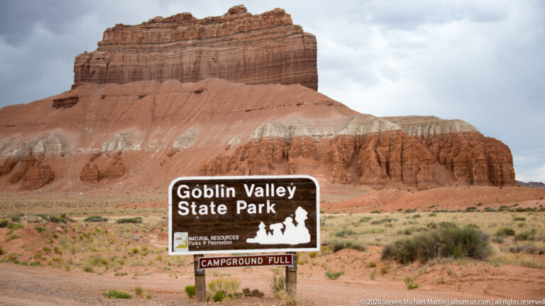 A Goblin Valley State Park sign with a “Campground Full” panel stands below a sandstone butte.