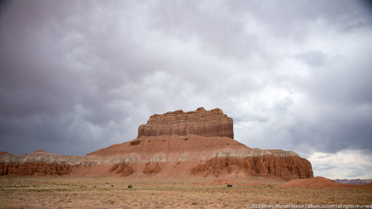 A flat-topped sandstone butte rises above a low red-rock plain beneath heavy clouds.