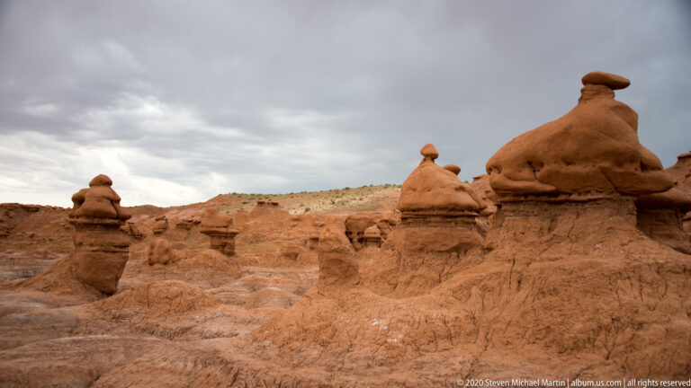 Large hoodoos in the foreground recede across a broad basin beneath dark storm clouds.