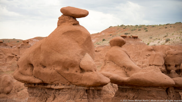 A wide sandstone cap overhangs a tapering pedestal, with smaller hoodoos behind it.
