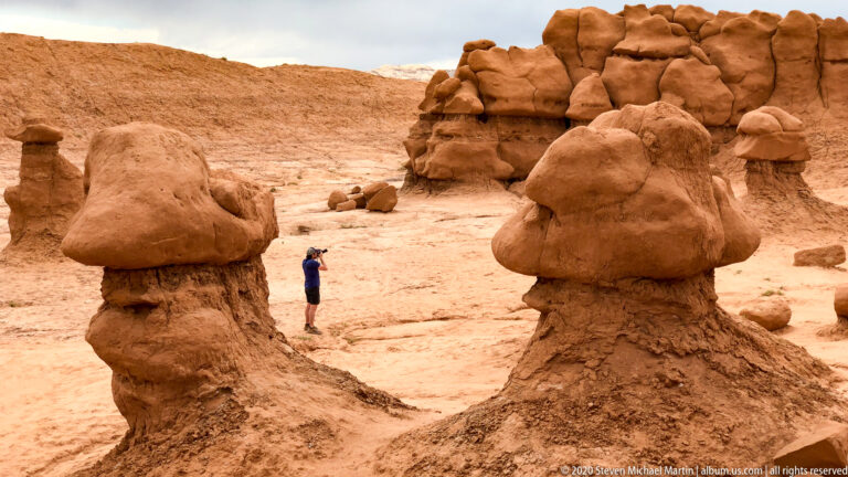 A visitor photographs the hoodoos while standing between two large capped sandstone pedestals.