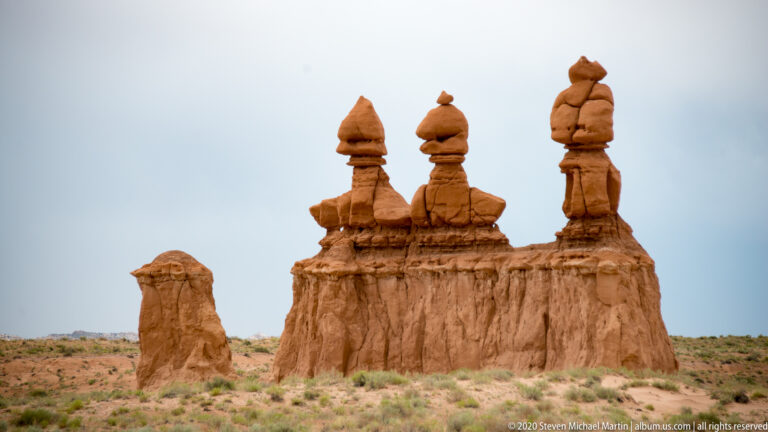 A group of hoodoo towers crowns a sandstone ledge, with one isolated pedestal in front.