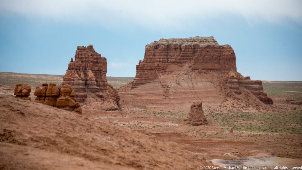 A narrow sandstone spire and broad mesa rise above an open valley, with smaller hoodoos to the left.