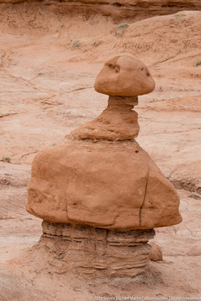 A small broad capstone balances on a short pedestal above rippled sandstone.