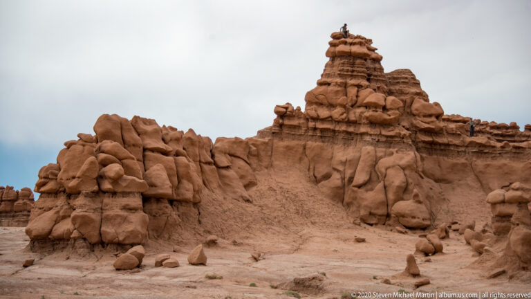 A tall sandstone pinnacle rises above a crowded ridge of rounded hoodoos and boulders.