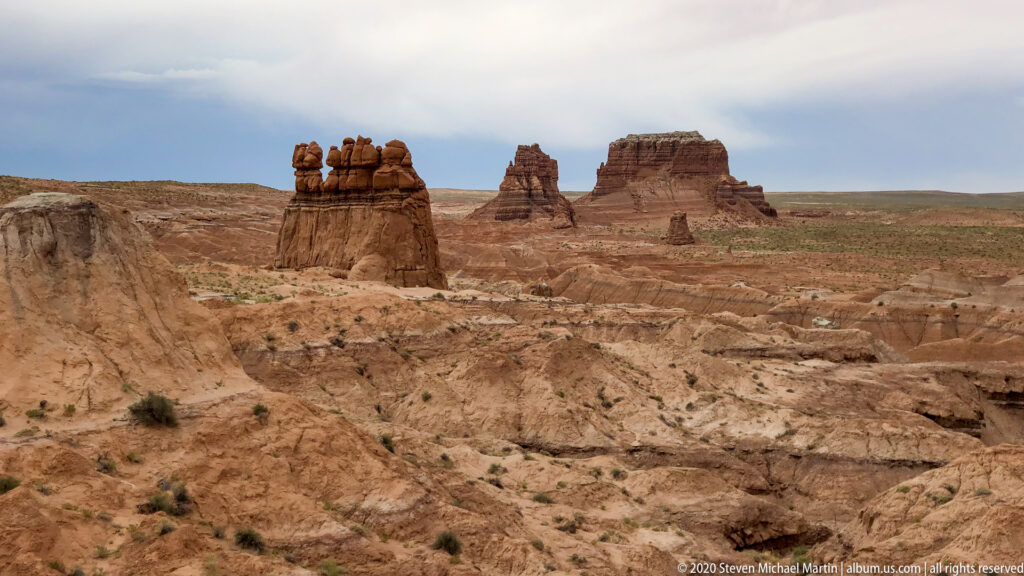 A wide dry valley dotted with sandstone towers stretches toward distant cliffs and mesas.