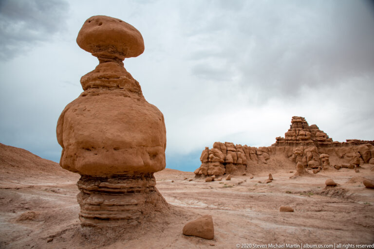 A large capped hoodoo stands in the foreground with smaller sandstone towers across the basin behind it.